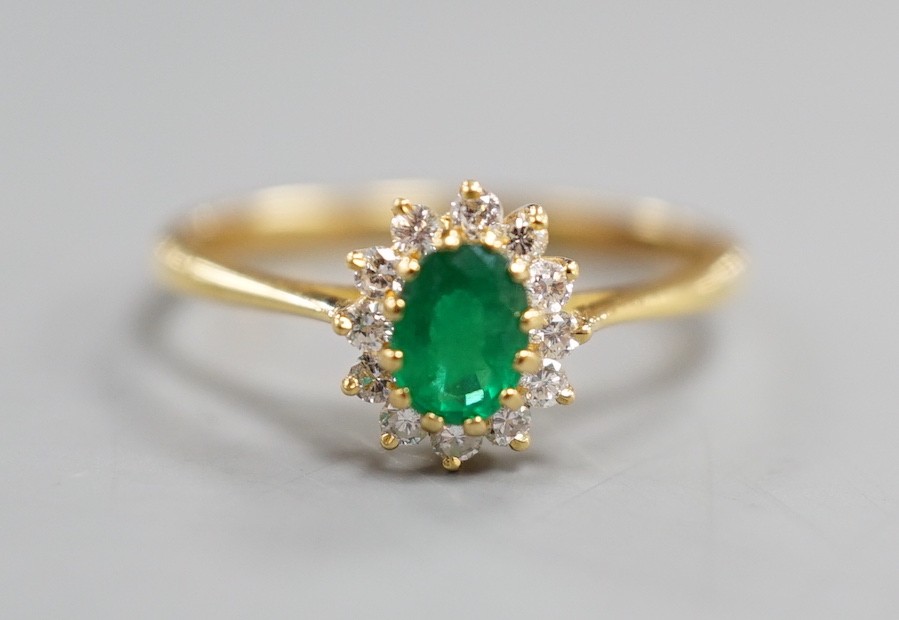 A modern 18ct gold, oval cut emerald and diamond chip set oval cluster ring, size N/O, gross weight 2.5 grams